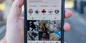 Hand holding a smartphone with an Instagram profile visible, set against a blurred street background.