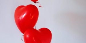 Three red heart-shaped balloons floating in a minimalist studio setting, evoking love and romance.