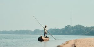 A solitary fisherman balances on a small boat in calm waters near a sandy shore at Bhubaneswar.