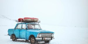 A vintage blue car with luggage on top amidst a snowy landscape in Kyrgyzstan.